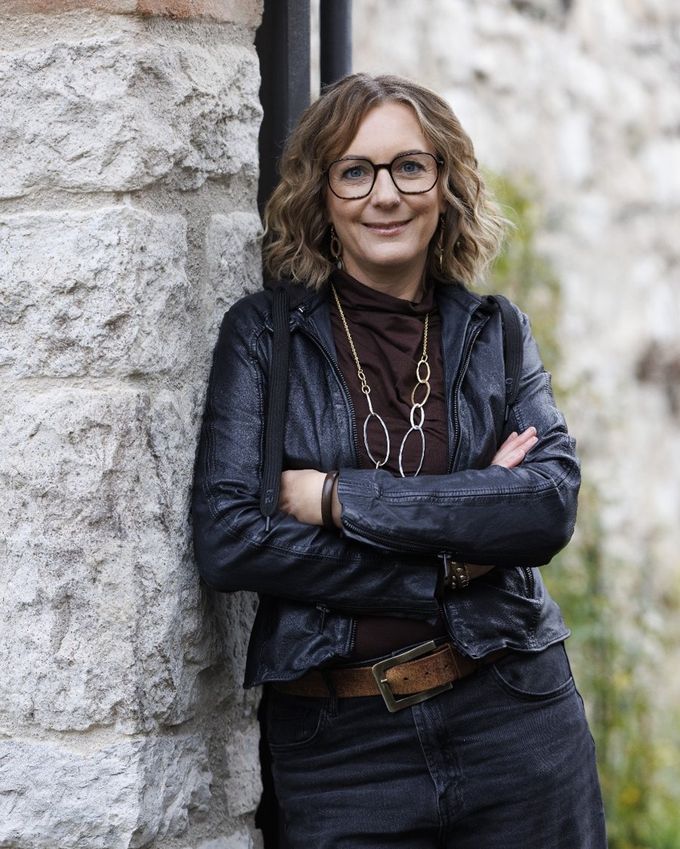 Andrea Tippelt, Heilpraktikerin für Frauenheilkunde und systemischer Coach, lächelnd an eine Steinmauer gelehnt